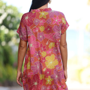 woman with brown hair wearing terracotta colored v neck shirt dress with large purple and yellow flowers