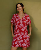 Woman in short sleeve shirt dress with pink floral print on red ground.