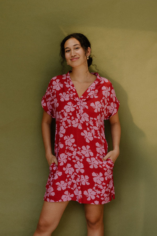 Woman in short sleeve shirt dress with pink floral print on red ground.