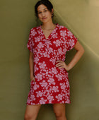 Woman in short sleeve shirt dress with pink floral print on red ground.