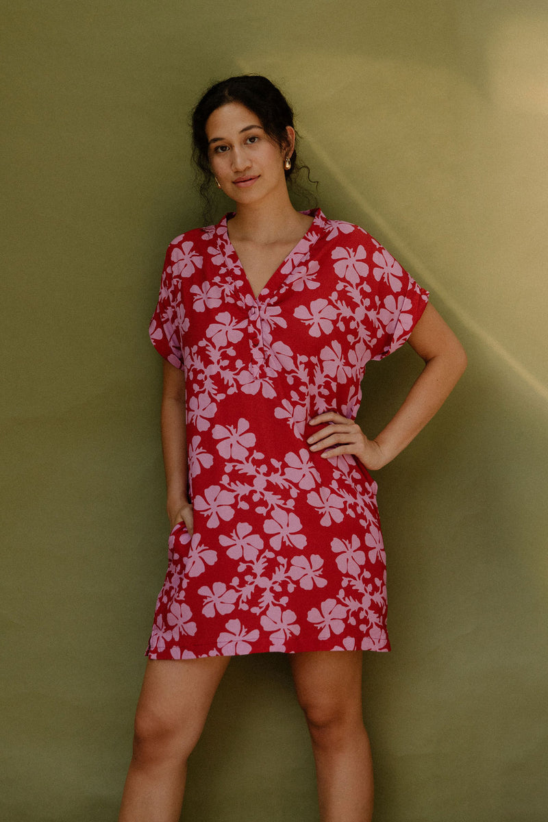 Woman in short sleeve shirt dress with pink floral print on red ground.