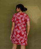 Woman in short sleeve shirt dress with pink floral print on red ground.