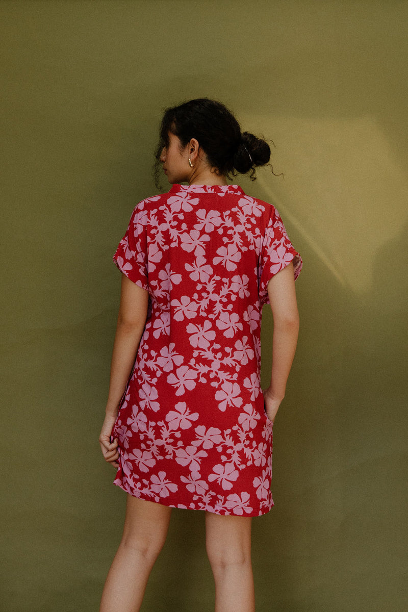 Woman in short sleeve shirt dress with pink floral print on red ground.