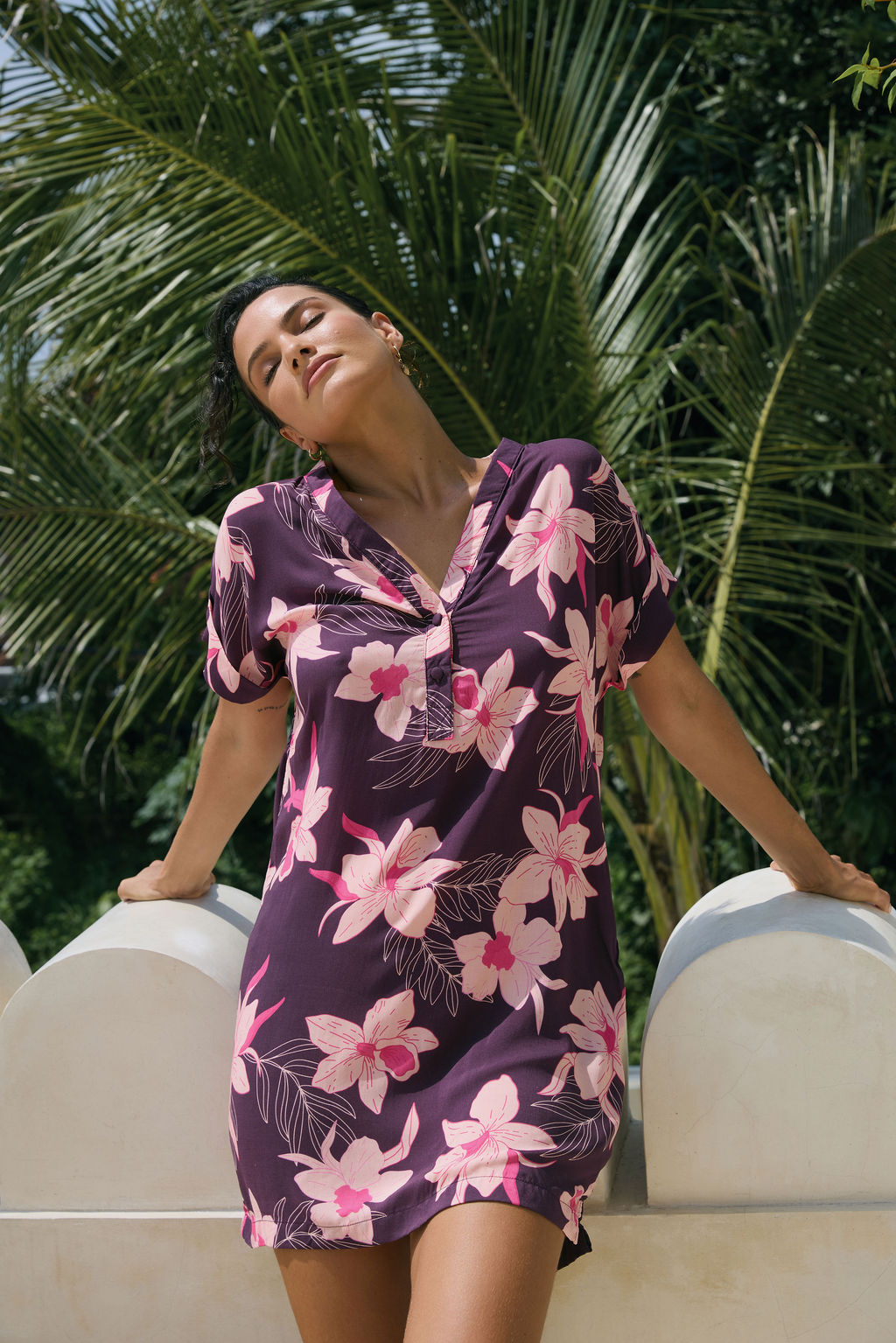 woman with brown hair wearing a dark purple short dress with button up v neck and orchid pattern
