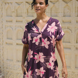 woman with brown hair wearing a dark purple short dress with button up v neck and orchid pattern