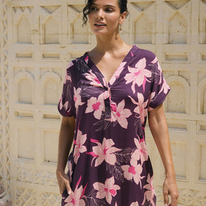 woman with brown hair wearing a dark purple short dress with button up v neck and orchid pattern