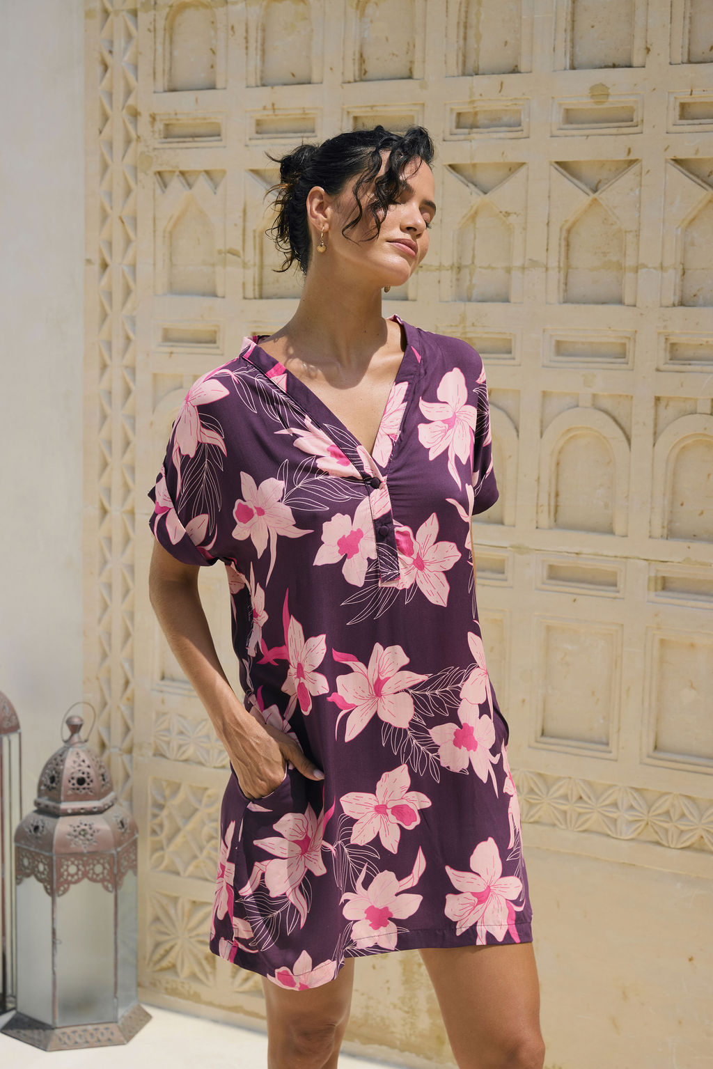 woman with brown hair wearing a dark purple short dress with button up v neck and orchid pattern
