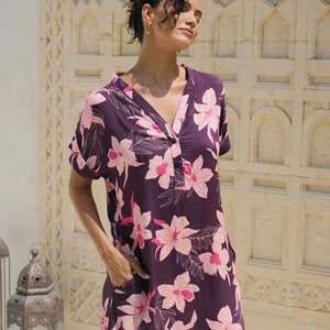 woman with brown hair wearing a dark purple short dress with button up v neck and orchid pattern