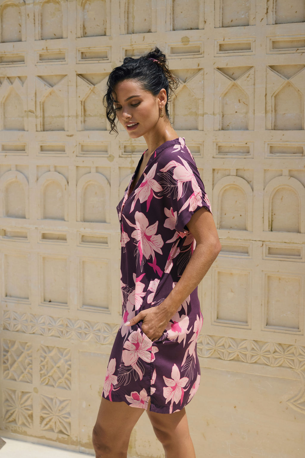 woman with brown hair wearing a dark purple short dress with button up v neck and orchid pattern