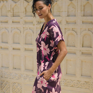 woman with brown hair wearing a dark purple short dress with button up v neck and orchid pattern
