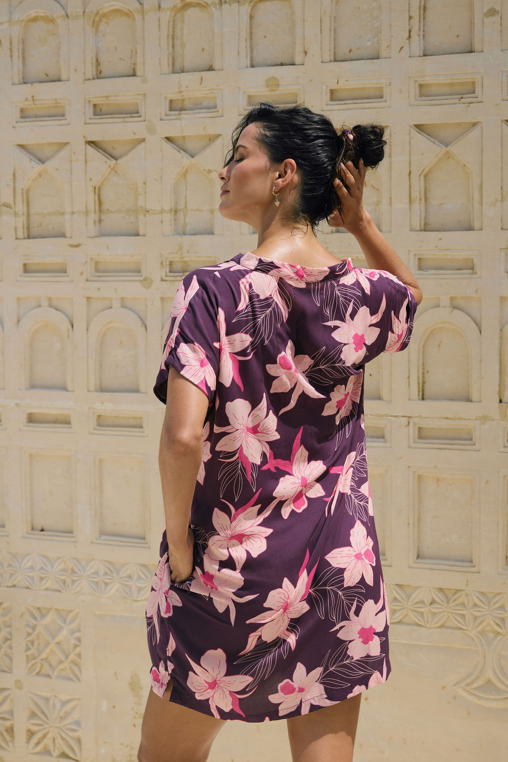 woman with brown hair wearing a dark purple short dress with button up v neck and orchid pattern