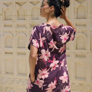 woman with brown hair wearing a dark purple short dress with button up v neck and orchid pattern