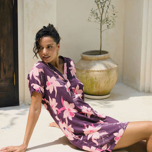 woman with brown hair wearing a dark purple short dress with button up v neck and orchid pattern