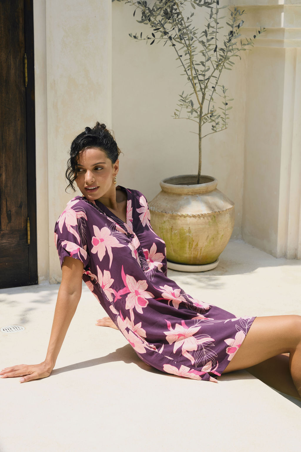 woman with brown hair wearing a dark purple short dress with button up v neck and orchid pattern