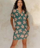 Woman in short sleeve shirt dress with pink floral on teal ground.