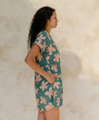 Woman in short sleeve shirt dress with pink floral on teal ground.