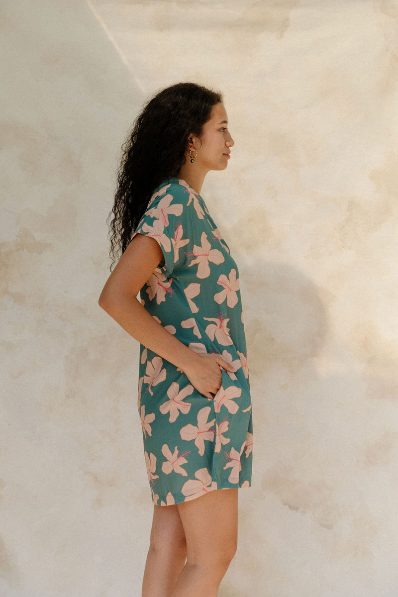 Woman in short sleeve shirt dress with pink floral on teal ground.