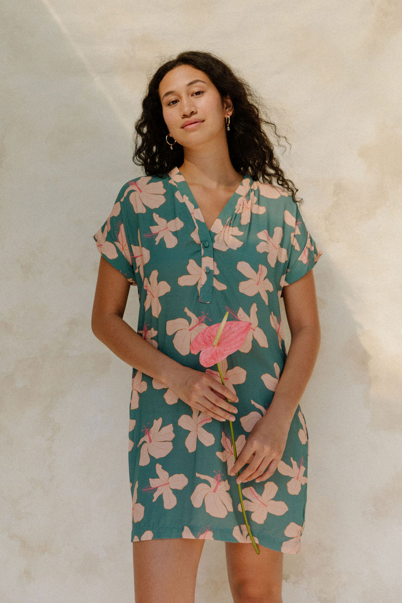 Woman in short sleeve shirt dress with pink floral on teal ground.