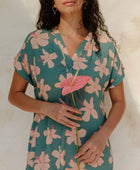 Woman in short sleeve shirt dress with pink floral on teal ground.