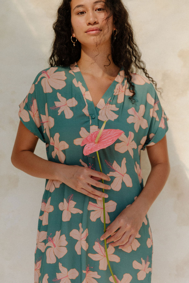 Woman in short sleeve shirt dress with pink floral on teal ground.