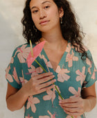 Woman in short sleeve shirt dress with pink floral on teal ground.