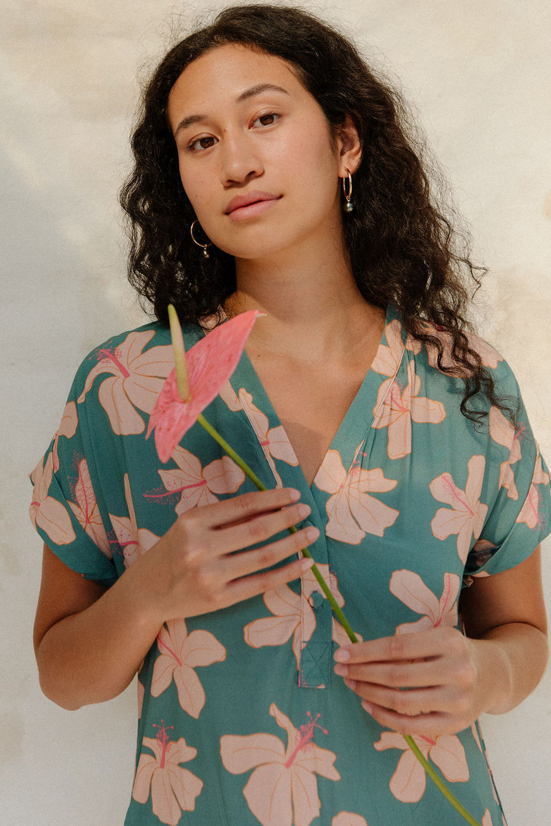 Woman in short sleeve shirt dress with pink floral on teal ground.