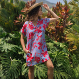 woman with brown hair wearing a mid length shirt dress with periwinkle background and bright red hibiscus print.