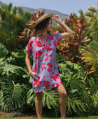 woman with brown hair wearing a mid length shirt dress with periwinkle background and bright red hibiscus print.