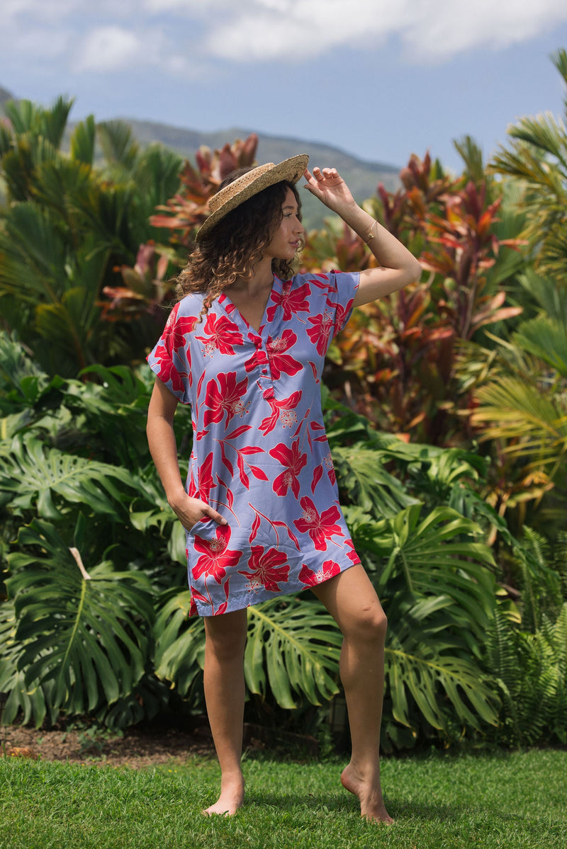woman with brown hair wearing a mid length shirt dress with periwinkle background and bright red hibiscus print.