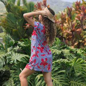 woman with brown hair wearing a mid length shirt dress with periwinkle background and bright red hibiscus print.
