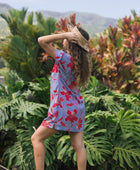 woman with brown hair wearing a mid length shirt dress with periwinkle background and bright red hibiscus print.