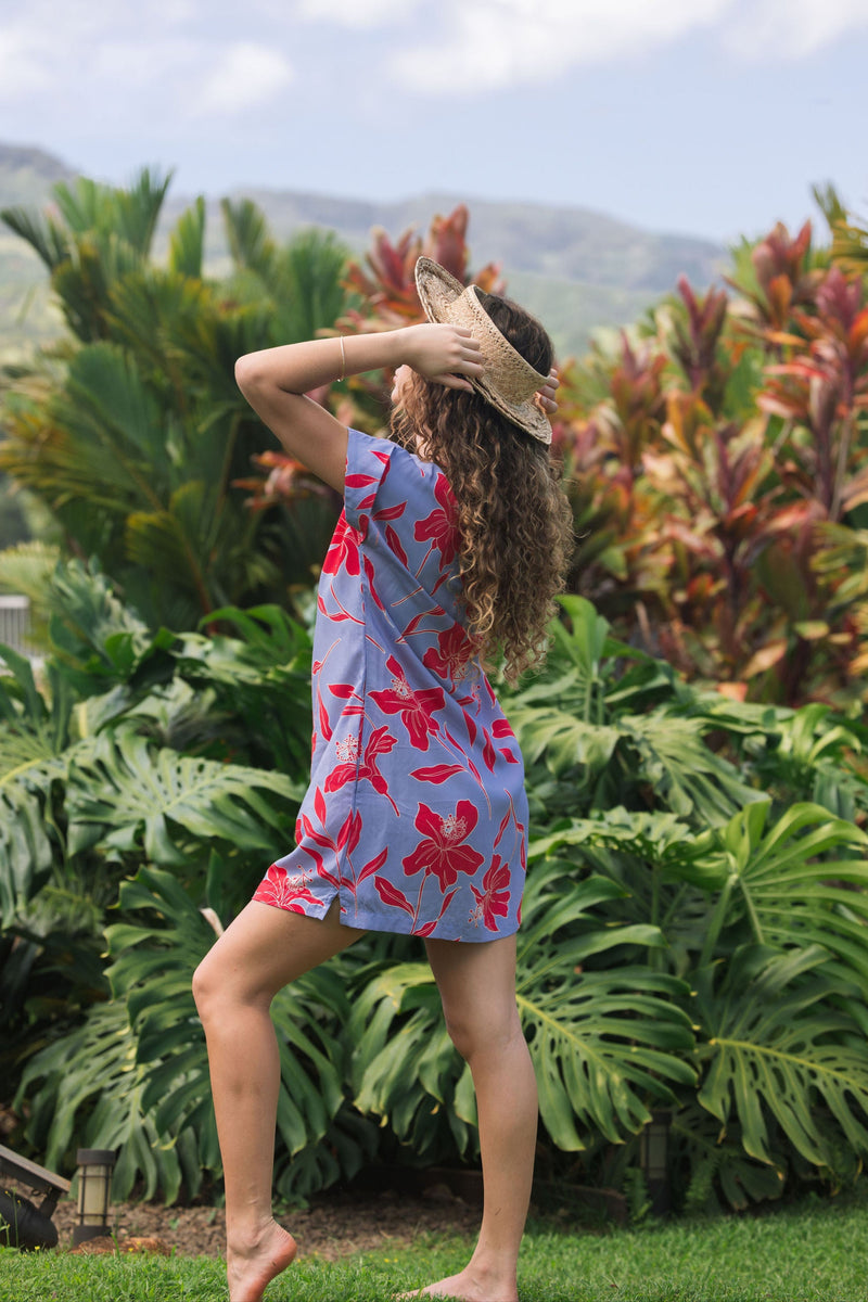 woman with brown hair wearing a mid length shirt dress with periwinkle background and bright red hibiscus print.