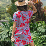 woman with brown hair wearing a mid length shirt dress with periwinkle background and bright red hibiscus print.