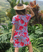 woman with brown hair wearing a mid length shirt dress with periwinkle background and bright red hibiscus print.
