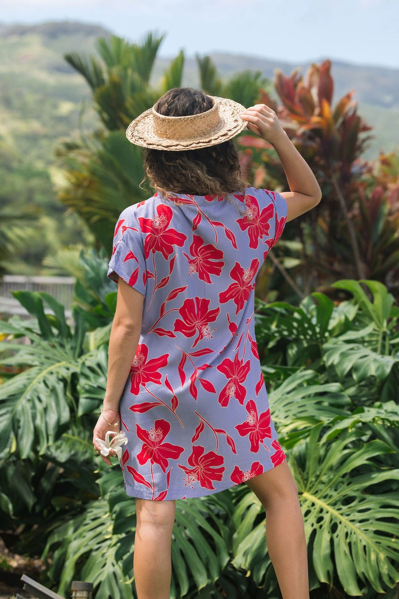 woman with brown hair wearing a mid length shirt dress with periwinkle background and bright red hibiscus print.