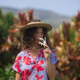 woman with brown hair wearing a mid length shirt dress with periwinkle background and bright red hibiscus print.