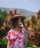woman with brown hair wearing a mid length shirt dress with periwinkle background and bright red hibiscus print.