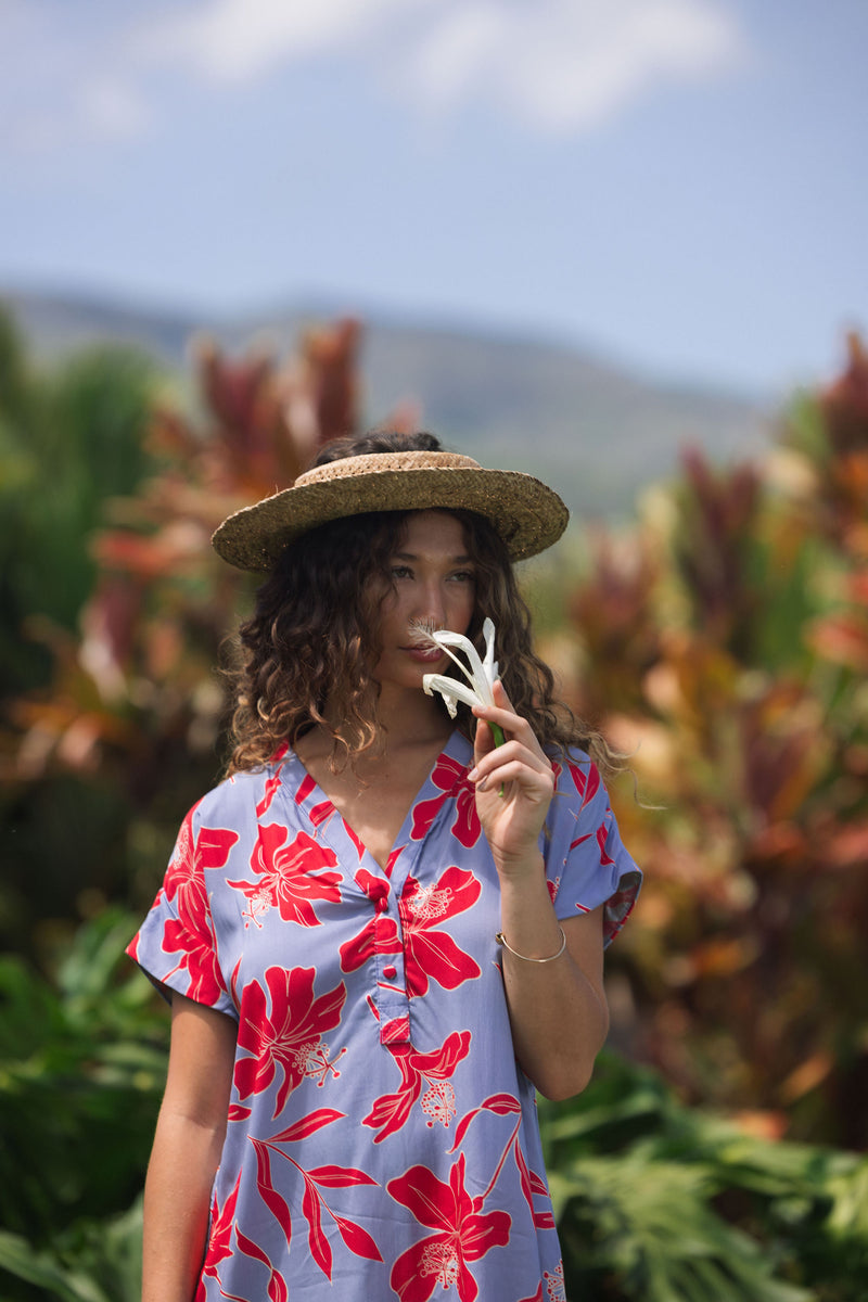 woman with brown hair wearing a mid length shirt dress with periwinkle background and bright red hibiscus print.