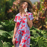 woman with brown hair wearing a mid length shirt dress with periwinkle background and bright red hibiscus print.
