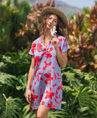woman with brown hair wearing a mid length shirt dress with periwinkle background and bright red hibiscus print.