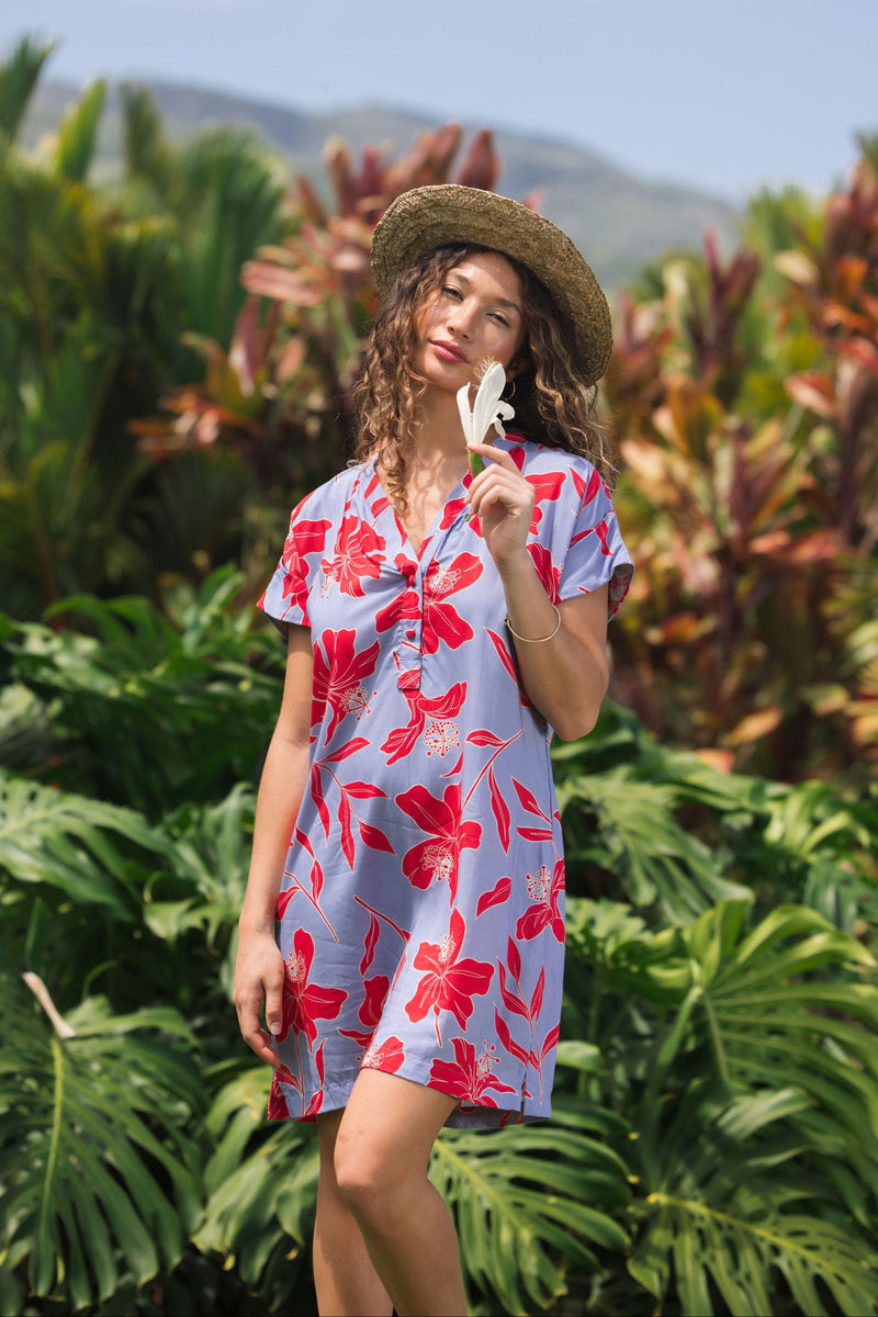 woman with brown hair wearing a mid length shirt dress with periwinkle background and bright red hibiscus print.