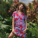 woman with brown hair wearing a mid length shirt dress with periwinkle background and bright red hibiscus print.
