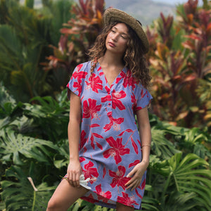 woman with brown hair wearing a mid length shirt dress with periwinkle background and bright red hibiscus print.
