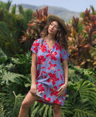 woman with brown hair wearing a mid length shirt dress with periwinkle background and bright red hibiscus print.