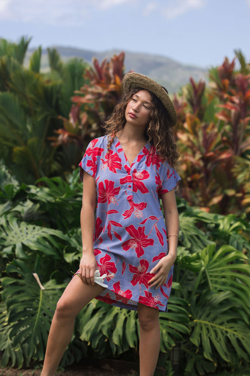 woman with brown hair wearing a mid length shirt dress with periwinkle background and bright red hibiscus print.