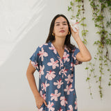 woman with black hair wearing a casual shirt dress with button up v neckline in a navy and pink hibiscus print. 