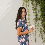 woman with black hair wearing a casual shirt dress with button up v neckline in a navy and pink hibiscus print. 