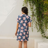 woman with black hair wearing a casual shirt dress with button up v neckline in a navy and pink hibiscus print. 