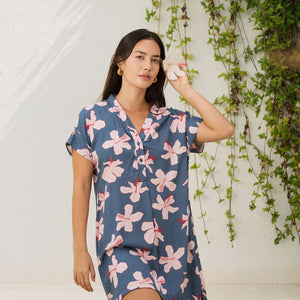 woman with black hair wearing a casual shirt dress with button up v neckline in a navy and pink hibiscus print. 