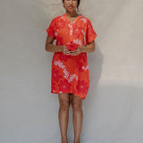 woman with brown hair wearing a retro orange v neck dress with flower pattern